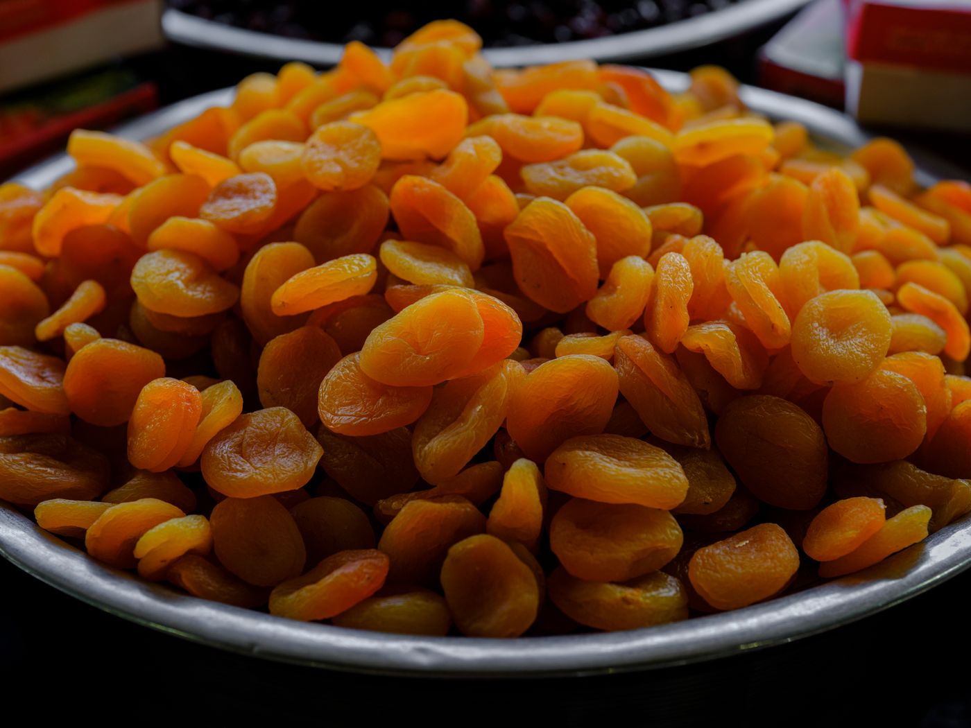 Dried apricots piled high in a metal bowl at a Xinjiang market stall