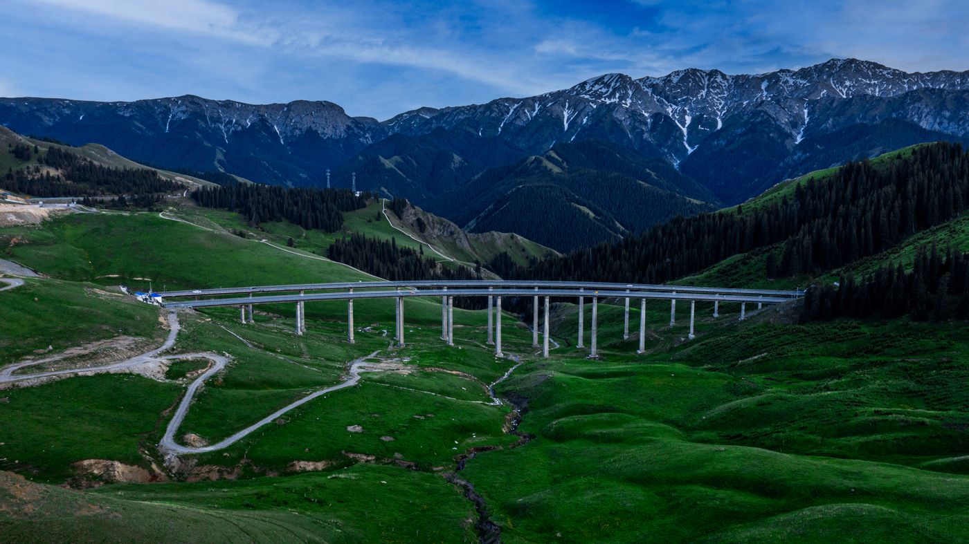 Aerial view of a highway viaduct crossing green mountain pastures in Xinjiang at dusk