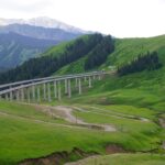 Elevated highway viaduct with vehicles crossing a green mountain valley in Xinjiang