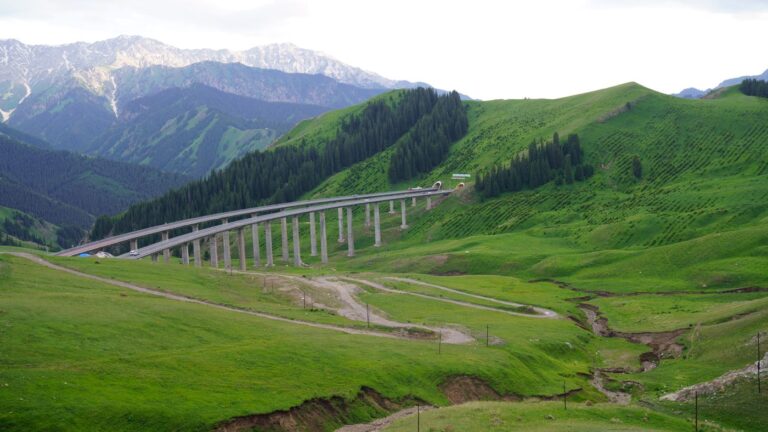 Elevated highway viaduct with vehicles crossing a green mountain valley in Xinjiang