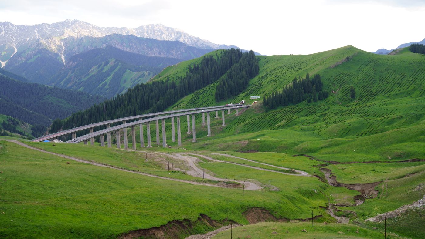 Elevated highway viaduct with vehicles crossing a green mountain valley in Xinjiang