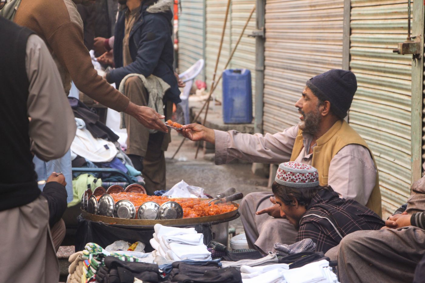 Vendor handing over a portion of orange halva sweets at a bazaar stall