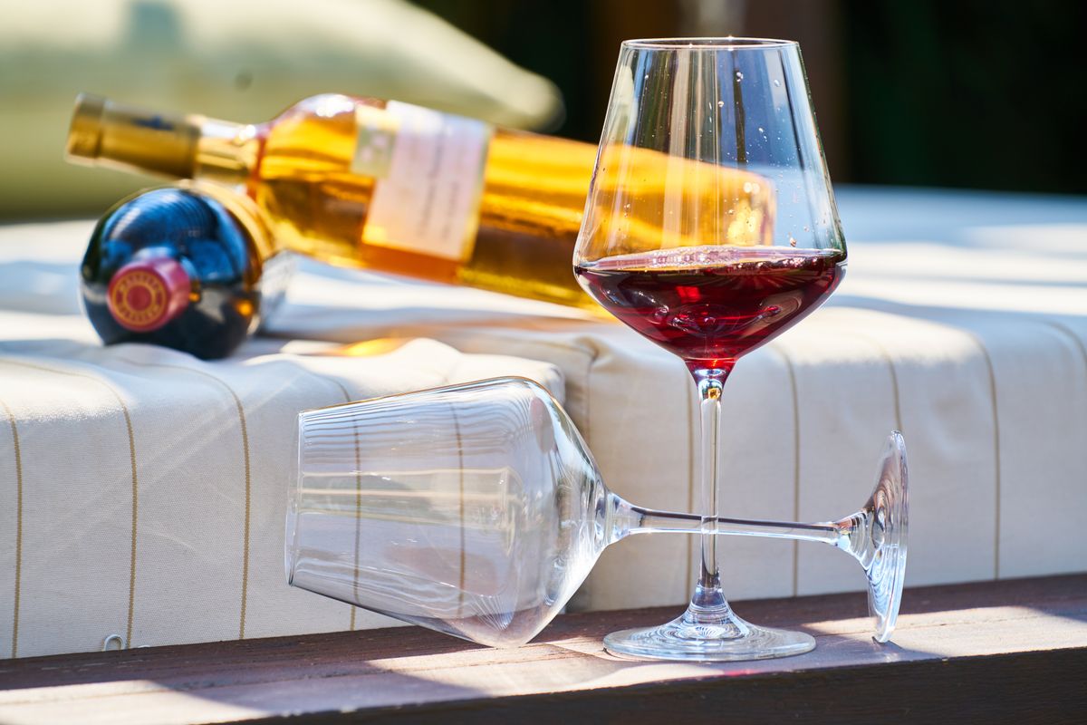 A glass of red wine with a bottle on a sunlit outdoor table